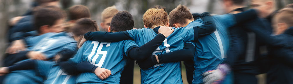 Eine Gruppe von Kindern beim Fußball Training. Kinder tragen blaue Trikots und umarmen sich
